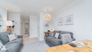 A modern living room with grey sofas, a wooden dining table, and a chandelier. - Sea Shells, St Ives – Sleeps 4 – On-Site Parking – Dog Friendly – Balcony (St Ives)