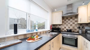 A modern kitchen with a large window, a stove, oven, and a sink. - Sea Shells, St Ives – Sleeps 4 – On-Site Parking – Dog Friendly – Balcony (St Ives)