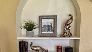 Uno scaffale decorato con oggetti ornamentali: una cornice con foto, una pianta, una scultura di pavone, libri e diversi piccoli oggetti.