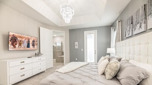 A bedroom with a large bed, a dresser, a chandelier, and artwork on the walls. - Sophisticated Villa with Movie Room at Encore (Kissimmee)