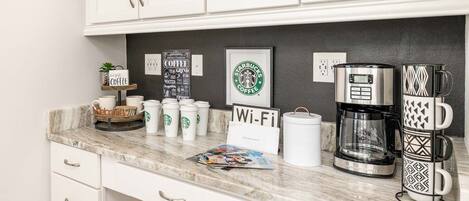 Una cocina con gabinetes blancos, una cafetera, un letrero de Wi-Fi y tazas de Starbucks.