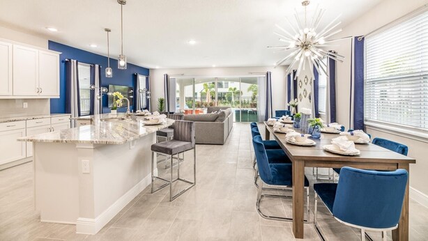 A modern kitchen with a central island, a dining area with blue chairs, and a bright chandelier. - Sophisticated Villa with Movie Room at Encore (Kissimmee)