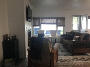 Ein Wohnzimmer mit Kamin, einer Couch, einem Sessel und einem Fenster mit Jalousien.