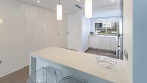 Une cuisine moderne avec des meubles blancs, un évier en acier inoxydable et des luminaires suspendus.