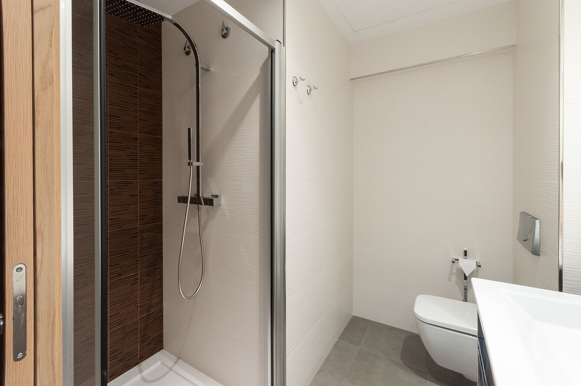 A modern bathroom with a glass-enclosed shower, a white toilet, and a wooden vanity.
