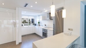 Une cuisine moderne avec des meubles blancs, des appareils en acier inoxydable et des luminaires suspendus.