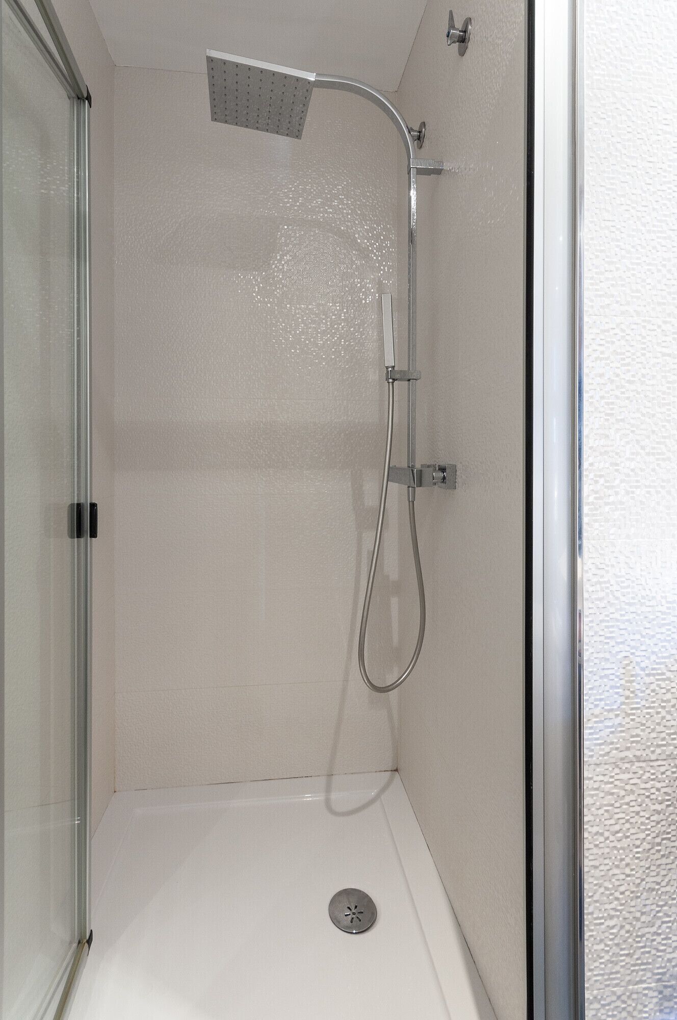 Une douche à l’italienne avec une porte en verre, un pommeau de douche et un flexible de douche.