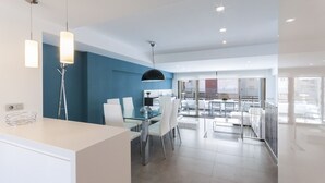 Une cuisine moderne avec une table à manger en verre, des chaises blanches et des luminaires suspendus.