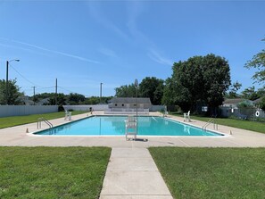A rectangular swimming pool with a diving board, surrounded by a grassy area and a white fence.
