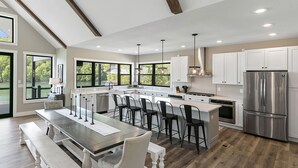 A modern kitchen with a central island, bar stools, and a stainless steel refrigerator.