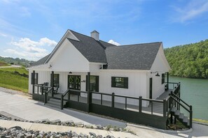 A modern house with a balcony overlooking a lake, a staircase leading to the entrance, and a well-maintained lawn.