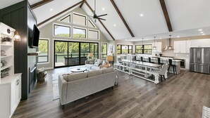 A spacious living area with a high ceiling, large windows, and a modern kitchen.