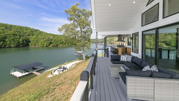 A deck with a sofa and a table, overlooking a lake and a dock.