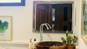 A bathroom with a wooden bowl sink, a mirror, a framed plant, and toiletries on the counter. - Central Stylish Home (Accra)