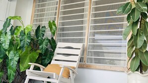 A white chair with a cushion, positioned next to a window with horizontal blinds. - Central Stylish Home (Accra)
