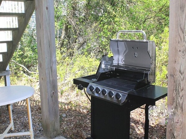 Un barbecue portatif doté de quatre brûleurs, installé à l’extérieur, avec une table en bois à proximité.