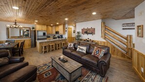 Un interior rústico con techo de madera, una cocina con alacenas de madera, un sofá de cuero y una escalera con barandillas de madera.