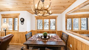 Un interior de madera con una mesa de comedor, sillas, una araña y ventanas amplias.