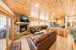 A cozy lodge interior with a stone fireplace, leather seating, a kitchen area, and a television displaying 'YELLOWSTONE.' - 6A Timberwolf lodge cabin vibe cozy stay with hot tub (Park City)