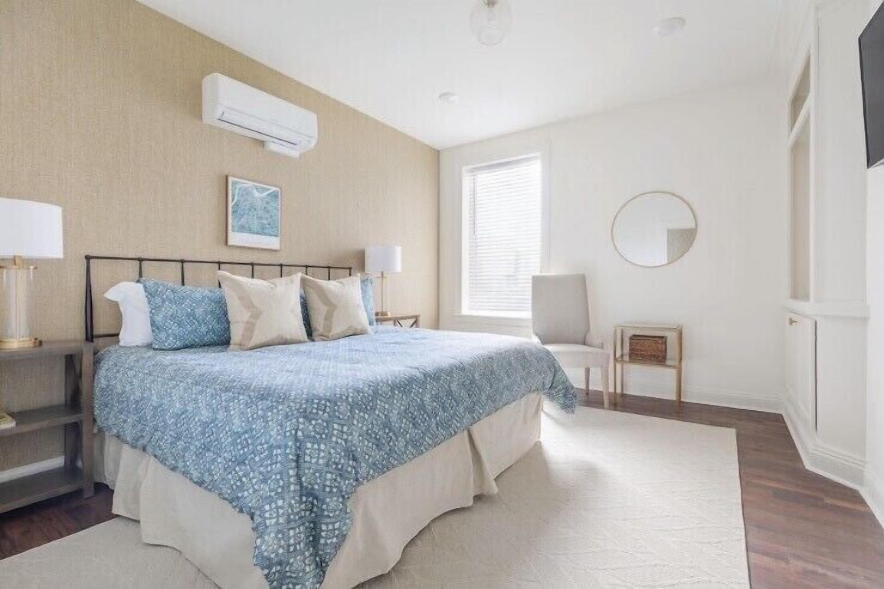 A bedroom with a bed, bedside tables, a chair, a small table, a mirror, and a window.