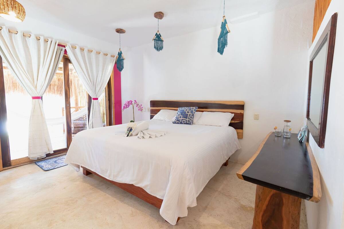 A bedroom with a wooden bed, white bedding, a small wooden table, and a hanging light fixture.