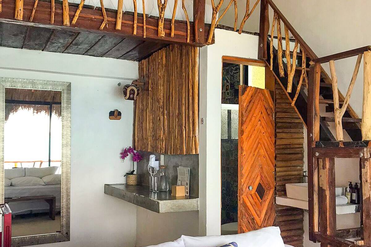 A bedroom with a bed, a wooden staircase, a small kitchenette, and a bathroom.