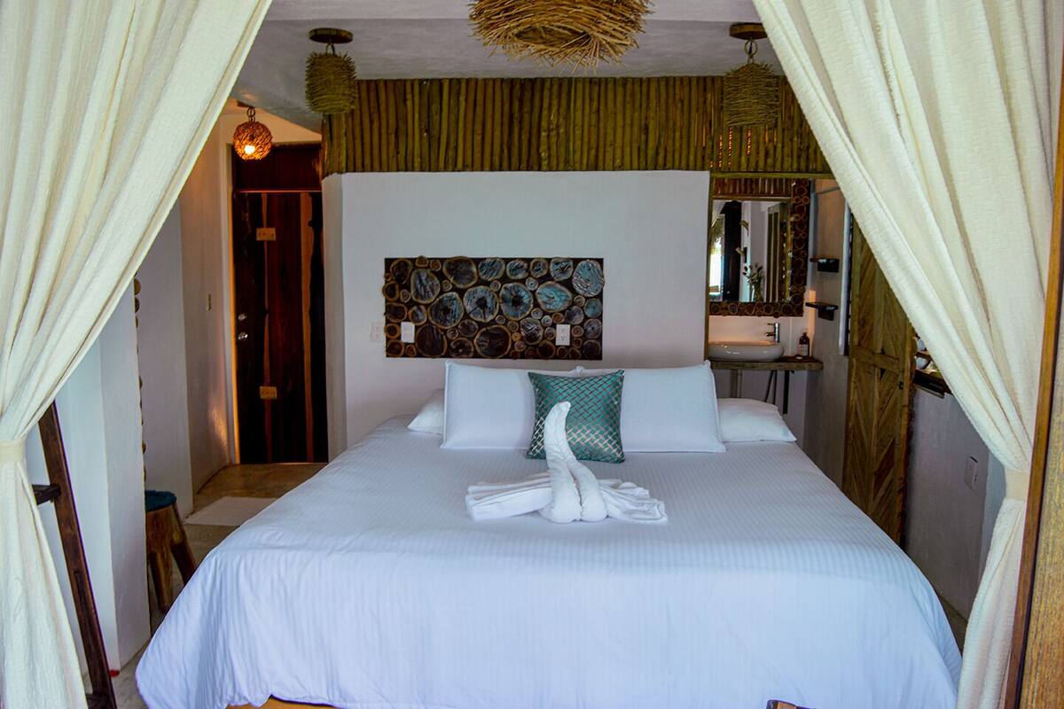 A hotel room with a bed, a wall-mounted artwork, a bathroom with a sink, and a door.