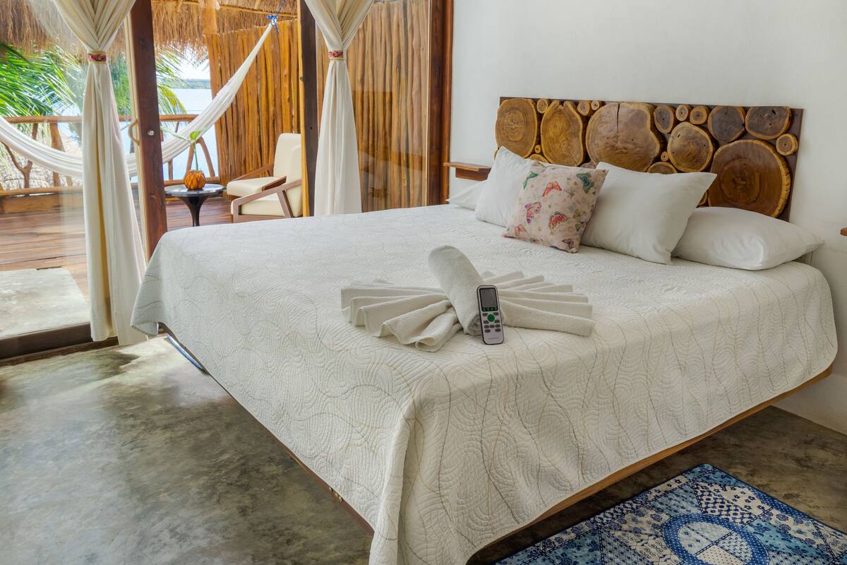 A neatly made bed with a remote control, a patterned rug, and a wooden headboard.