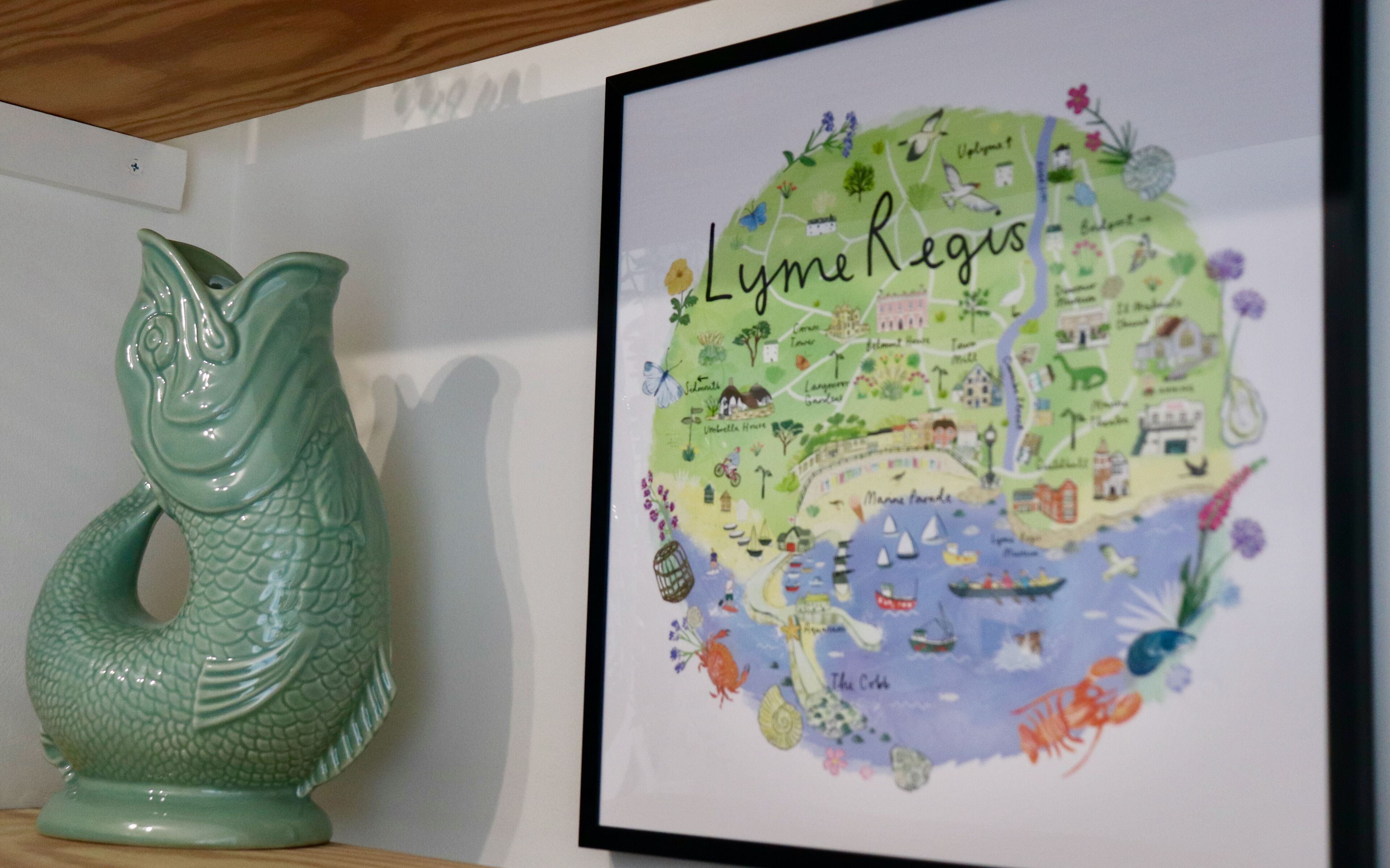 Un mapa enmarcado de Lyme Regis con ilustraciones de puntos de referencia locales y una escultura de pez de cerámica verde.