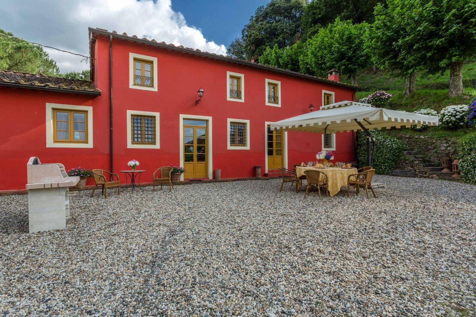 A red building with a gravel courtyard, outdoor seating, and a covered table area.