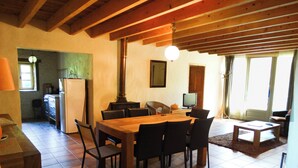A dining area with a wooden table and chairs, a kitchen in the background, and a window with curtains. - La Maison d'Aum -Perigord Dordogne between Bergerac and Perigueux- 8pers-Pool (Bourrou)