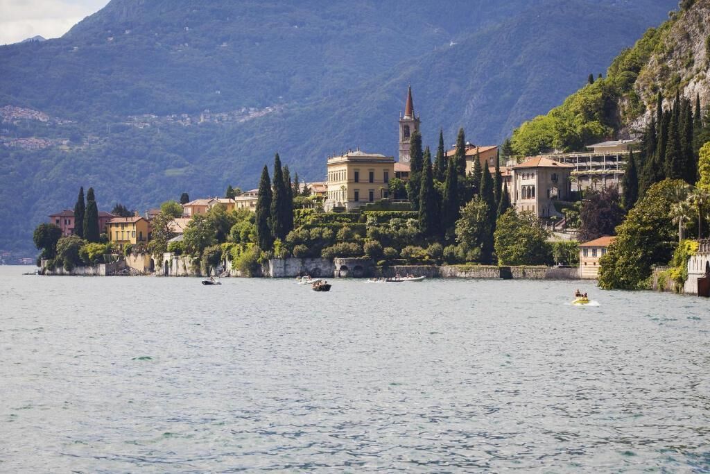 A lakeside town with historic buildings, a prominent church tower, and a clear view of the surrounding mountains.