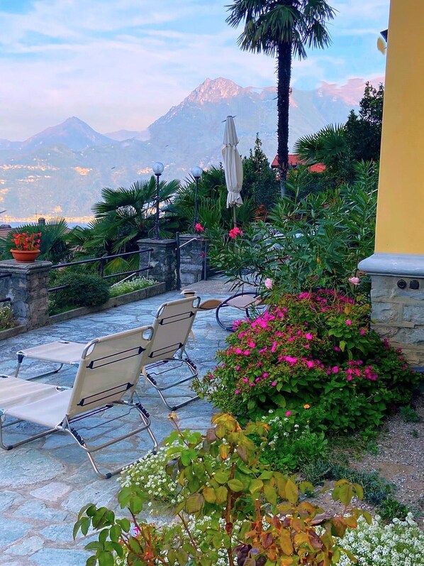 A patio with two lounge chairs, a stone pathway, and a view of mountains. - VILLA SILVANA - DOUBLE ROOM WITH LAKE VIEW (PERLEDO)