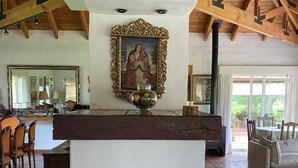 Un'ampia zona giorno con soffitto in legno, un grande specchio, un caminetto con una ciotola decorativa e una panca in legno intagliata.