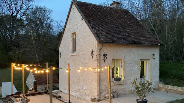 Una casa de piedra con techo inclinado, un pequeño porche y una guirnalda de luces.