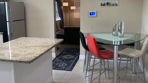 Une cuisine moderne dotée de plans de travail en granit, d’un réfrigérateur en acier inoxydable et d’une table à manger en verre avec des chaises en métal.