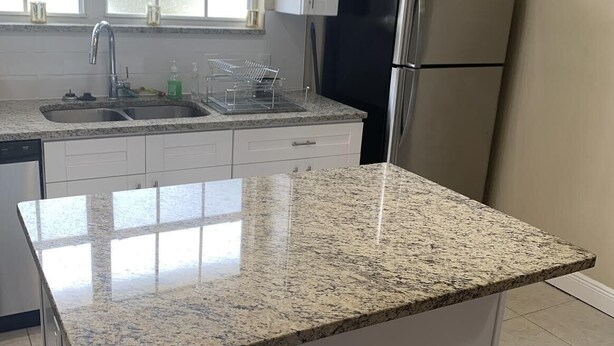 Une cuisine dotée d’un plan de travail en granit, d’appareils électroménagers en acier inoxydable, de meubles blancs et d’un éclairage suspendu.