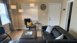 Un salon moderne avec un canapé d’angle noir, une lampe sur pied, une petite table d’appoint et un fauteuil avec un coussin jaune.