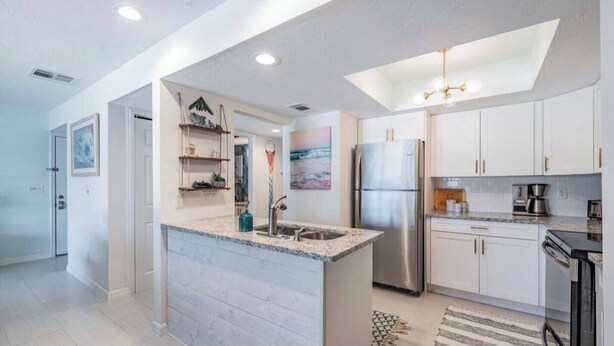 Una cocina moderna con armarios blancos, un refrigerador de acero inoxidable y una encimera de granito.