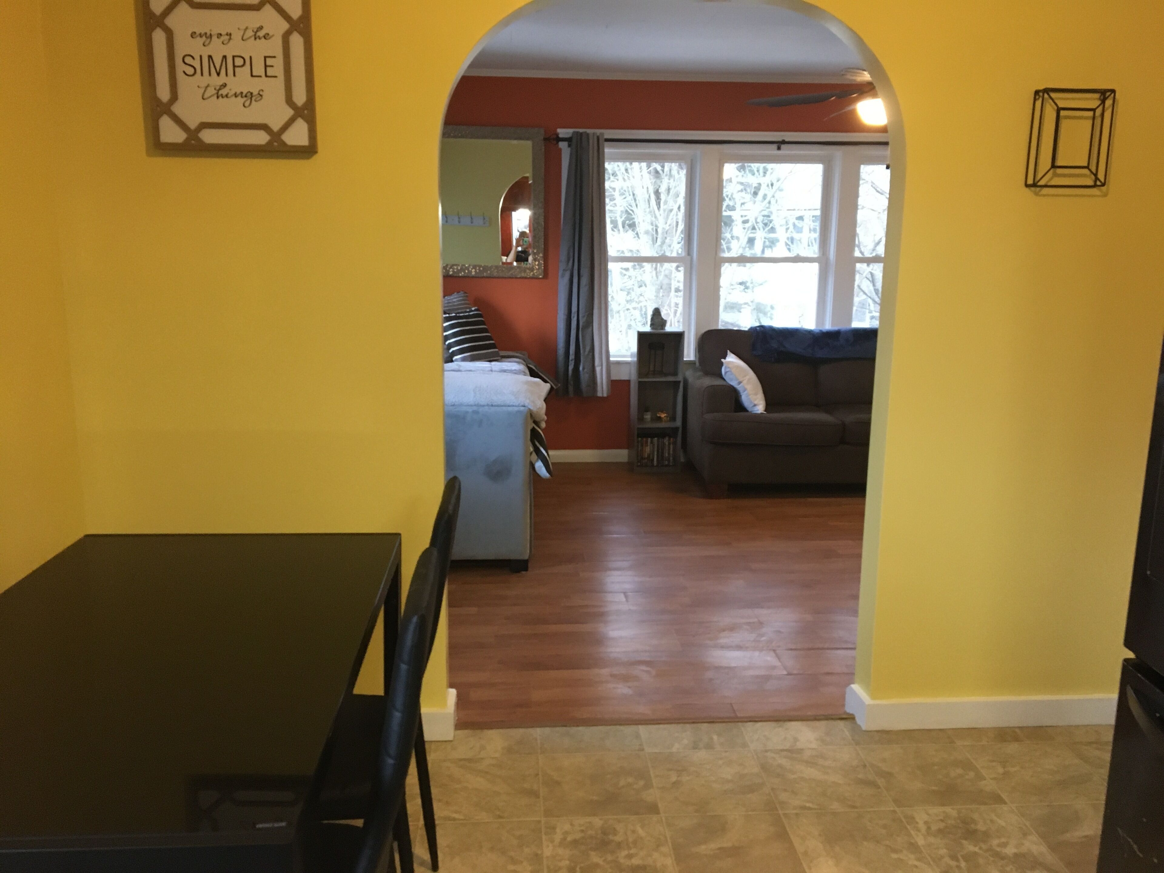 A living room with a sofa, a dining table with chairs, and a kitchen area visible through an archway.