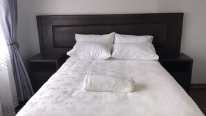 Ein ordentlich bezogenes Bett mit weißer Bettdecke und Kissen, flankiert von dunklen Nachttischen.
