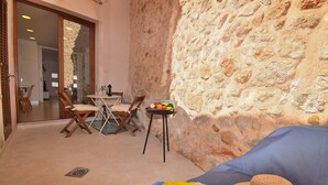 A cozy room with a stone wall, a dining area with chairs and a table, and a bed with a hat on it.