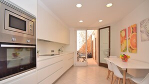 A modern kitchen with built-in appliances, a dining area with white chairs, and a view of the outdoors.