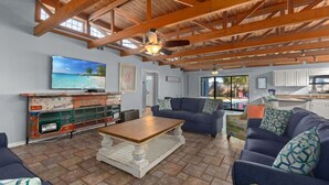 A spacious living area with a high ceiling, rustic wooden beams, a large TV, and a vintage car display.
