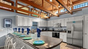 A spacious kitchen with a large island, white cabinets, stainless steel appliances, and a high ceiling with exposed beams.