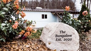 A stone marker with "The Bungalow Est. 2020" engraved, surrounded by autumn foliage and a house in the background. - Couples Romantic Country Bungalow, Private, Stock Tank Pool, Birds, Wildlife (Vandalia)