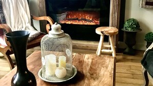 A cozy living room with a fireplace, a wooden coffee table, a vase, a candle holder, and a small stool.