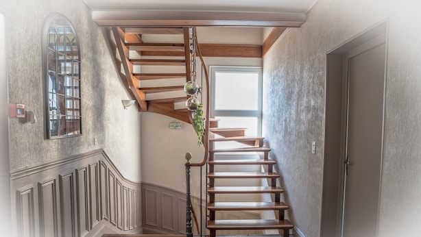 A wooden staircase with a glass door at the top, a wall-mounted light fixture, and a window with a view of the outdoors.