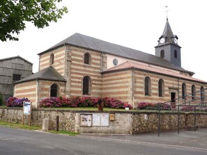 Una iglesia histórica con un campanario, muros de piedra y macizos de flores.