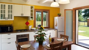 Une cuisine moderne avec des meubles blancs, une table à manger pour quatre personnes et une vue sur le jardin grâce à la porte-fenêtre coulissante.
